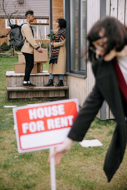 A person, dressed in light-colored clothing, is seen in an indoor space handling a cardboard box, preparing it for a home relocation process. They are placing the box on top of other similarly packed